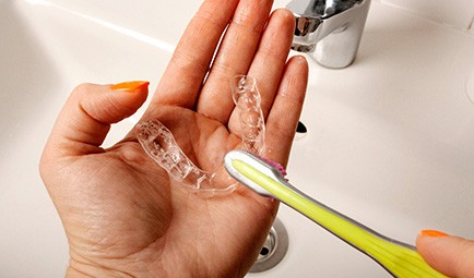 A woman brushing her nightguard with a toothbrush
