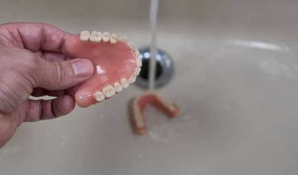 Hand holding denture above sink