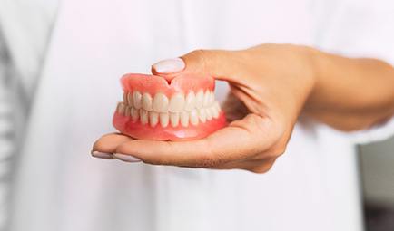 Closeup of dentist holding dentures in Baltimore