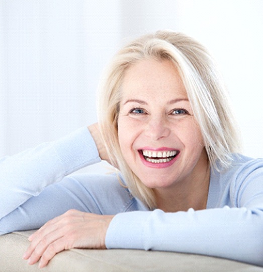 White-haired woman leaning on couch and smiling with dentures in Baltimore, MD