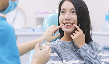 Woman in dentist’s chair pointing to tooth