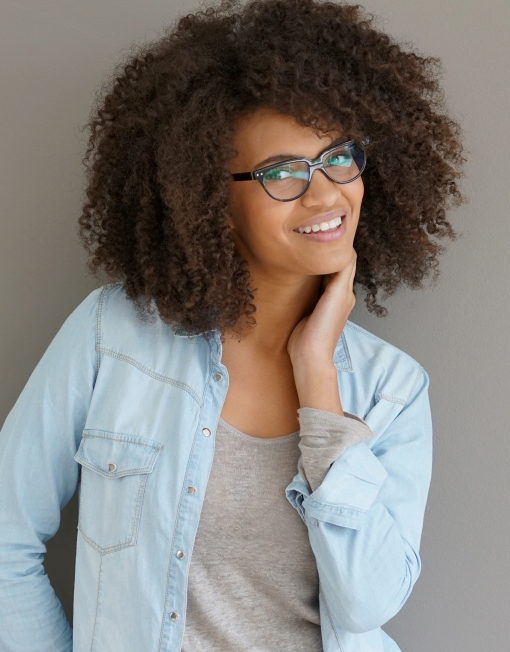 Woman in denim shirt smiling and holding her head in her hand