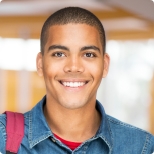 Young man in denim shirt grinning in front of windows