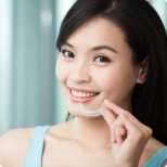Smiling woman holding Invisalign orthodontic aligner