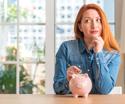 Woman putting coin in piggy bank for Invisalign in Baltimore