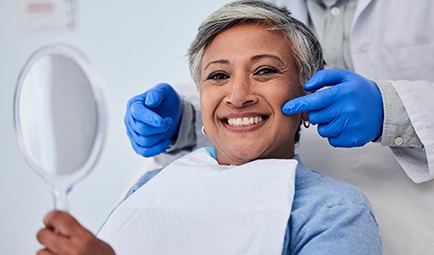 Woman smiling while holding handheld mirror at dentist's office