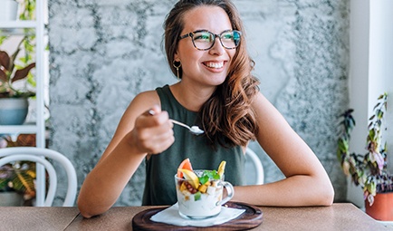 Woman with glasses smiling while eating breakfast at home