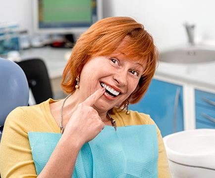 Woman pointing to smile after full mouth reconstruction