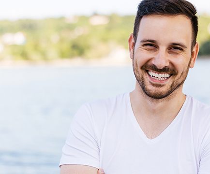 Man in white shirt by lake smiling with veneers