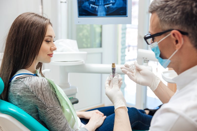 a dentist showing a female patient what a dental implant looks like and explaining how it works