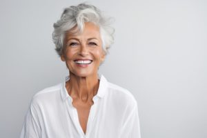 Woman with gray/white hair in a white shirt smiling in front of a gray background