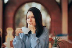 Woman holding coffee cup, experiencing sensitivity in her dental implant