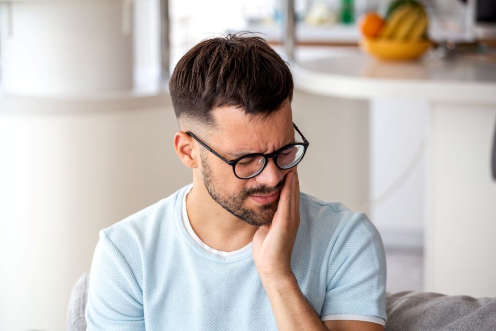 Man in glasses looking down holding hand to jaw in pain