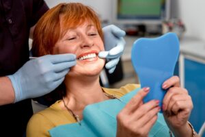 Dental patient looking at her new implants in mirror sitting in dentist’s chair.